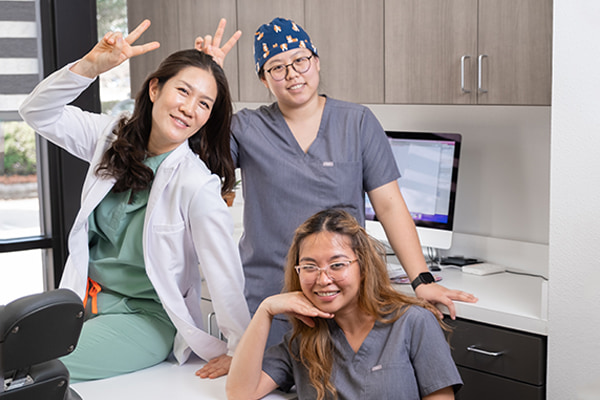 Dr. Sooyoun smiling in her dental office with her two dental assistants as they make the peace and love sign